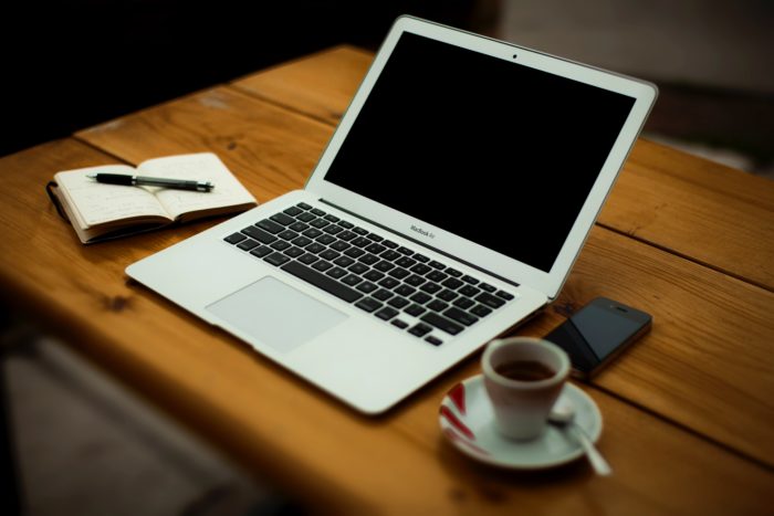 macbook laptop on a table with a coffee cup and an open notepad