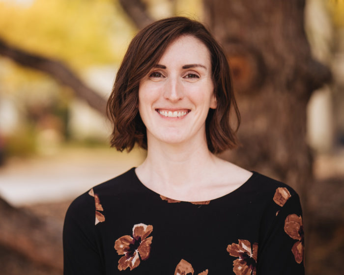 woman smiling with a tree and fall leaves in the background